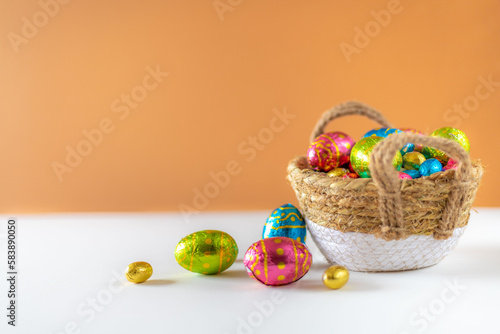 Easter eggs in basket with cream background on white table. Studio lighting colorful easter decorated eggs for egg hunt with wicker basket and flowers. Banner for web and composition. Wishes card photo