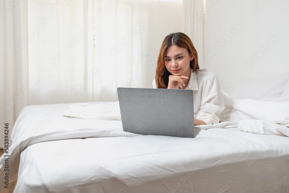 Woman in white nightgown waking up on weekend morning resting and relaxing playing with laptop mobile phone Eating bread and drinking tea in glass inside white bedroom. Morning vacation concept. Woman in white nightgown waking up on weekend morning resting and relaxing playing with laptop mobile phone Eating bread and drinking tea in glass inside white bedroom. Morning vacation concept.