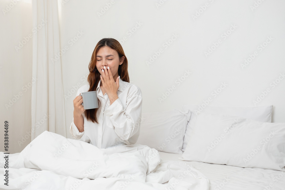 Woman in white nightgown waking up on weekend morning resting and relaxing playing with laptop mobile phone Eating bread and drinking tea in glass inside white bedroom. Morning vacation concept. Woman in white nightgown waking up on weekend morning resting and relaxing playing with laptop mobile phone Eating bread and drinking tea in glass inside white bedroom. Morning vacation concept.