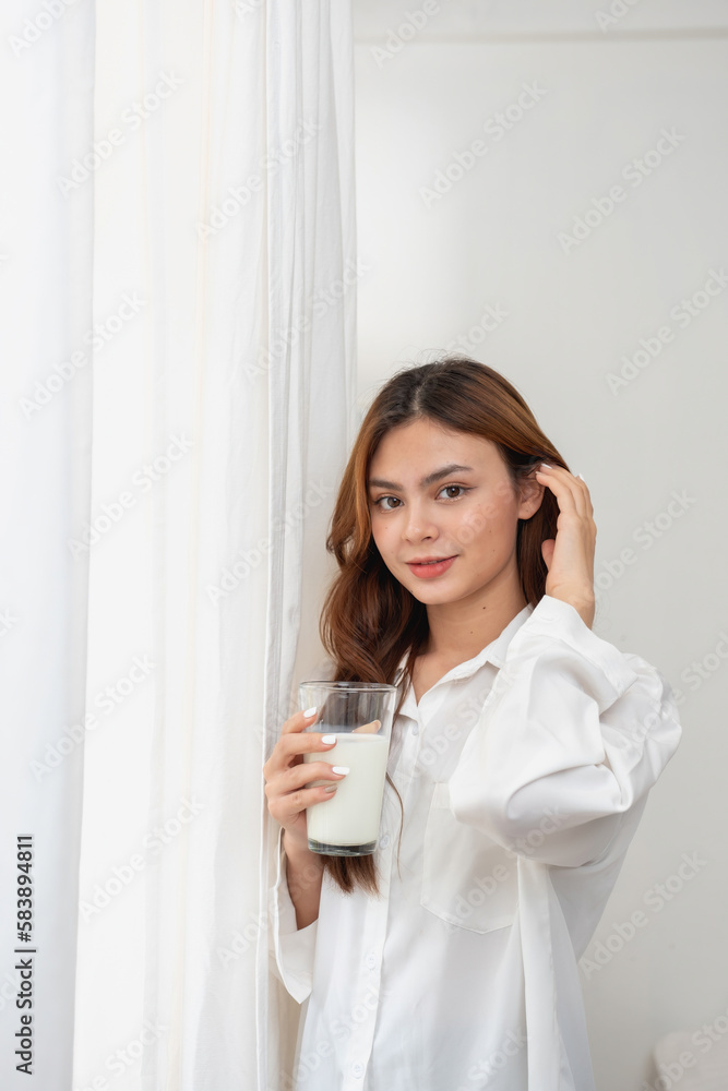 Woman in white nightgown waking up on weekend morning resting and relaxing playing with laptop mobile phone Eating bread and drinking tea in glass inside white bedroom. Morning vacation concept. Woman in white nightgown waking up on weekend morning resting and relaxing playing with laptop mobile phone Eating bread and drinking tea in glass inside white bedroom. Morning vacation concept.