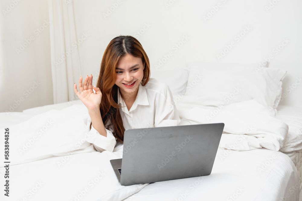 Woman in white nightgown waking up on weekend morning resting and relaxing playing with laptop mobile phone Eating bread and drinking tea in glass inside white bedroom. Morning vacation concept. Woman in white nightgown waking up on weekend morning resting and relaxing playing with laptop mobile phone Eating bread and drinking tea in glass inside white bedroom. Morning vacation concept.
