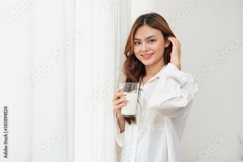 Woman in white nightgown waking up on weekend morning resting and relaxing playing with laptop mobile phone Eating bread and drinking tea in glass inside white bedroom.  Morning vacation concept.