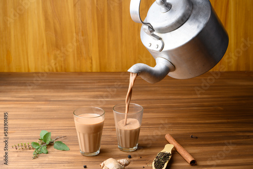 фотографія indian masala chai or tea in traditional glasses, with kettle, spices and tea leaves on dark, wooden background