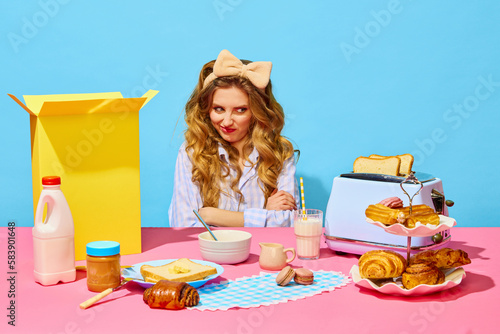 Portrait of funny redheaded girl wearing bow and grimacing simbolizing dislike to food on pink tablecloth over light blue background photo