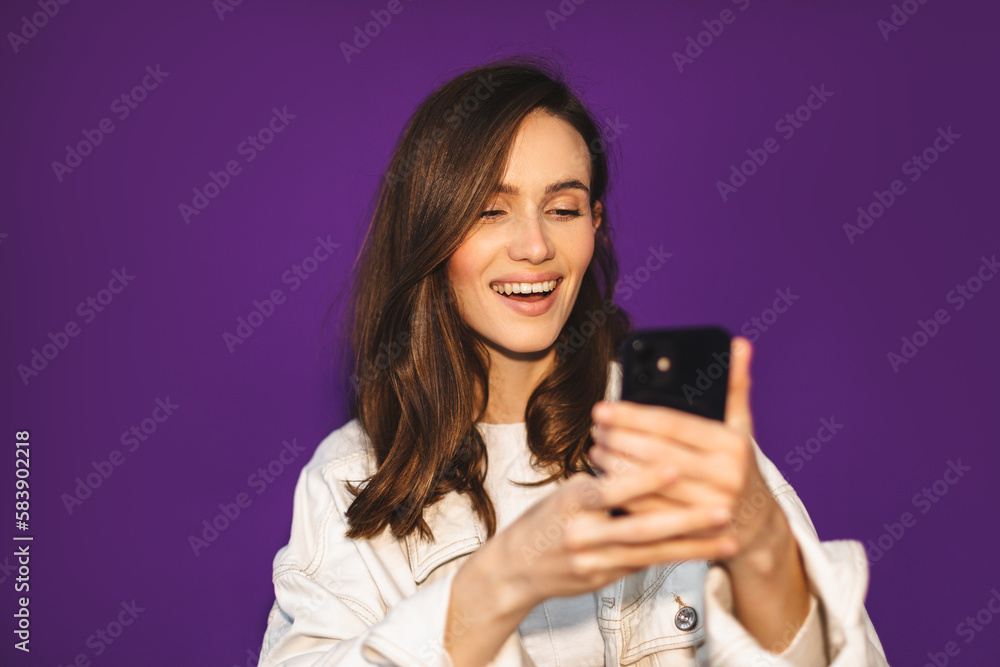 Photo of cute pretty young lady wear jeans denim white jacket reading message modern gadget isolated violet color background. Photo of cute pretty young lady wear jeans denim white jacket reading message modern gadget isolated violet color background.