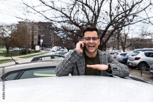 Young nervous business man standing by his car after working hours talking on the phone arguing with employees because he has to go back to work to correct their mistake. Cant exit parking space lot © Srdjan