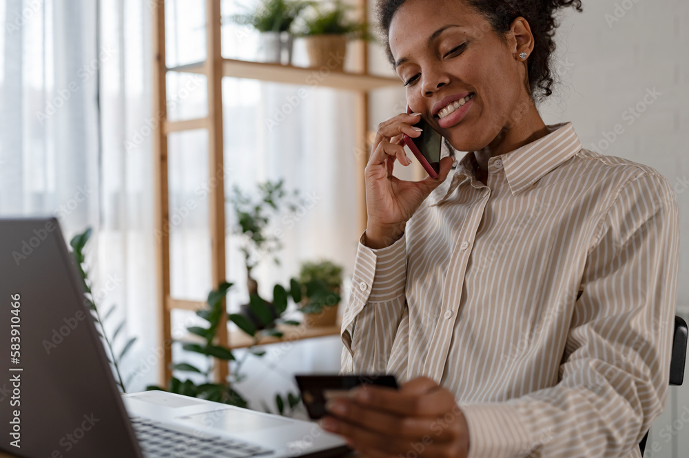 Young smiling cheerful African woman paying with credit card over internet. Online banking app using. Internet shopping. Young smiling cheerful African woman paying with credit card over internet. Online banking app using. Internet shopping.