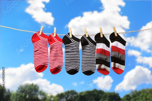 Clean washed striped socks hanging on clothesline to dry outdoors on sunny summer day. Clothesline with red, gray and white socks against blue sky.