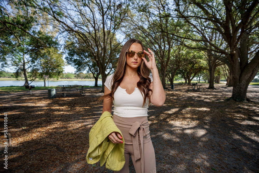 Flash photo of a woman adjusting her sunglasses posing in a nature park setting Flash photo of a woman adjusting her sunglasses posing in a nature park setting