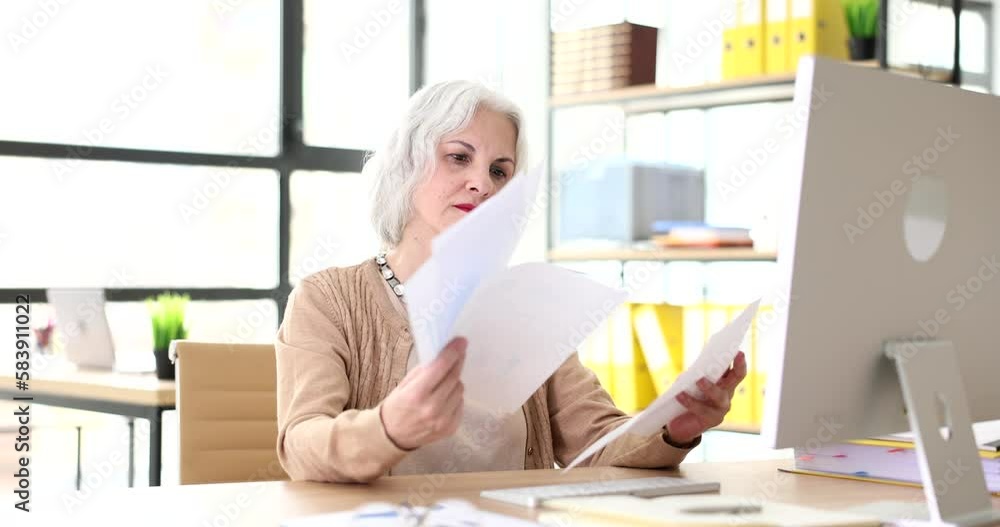 Elderly woman with gray hair studying documents at desk in office 4k movie slow motion Elderly woman with gray hair studying documents at desk in office 4k movie slow motion