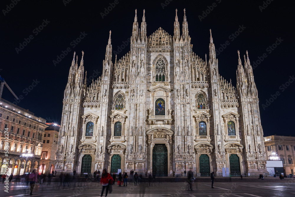 Milan, Italy low angle wide shot of illuminated gothic style Roman Catholic Duomo Cathedral facade at the homonym main square.