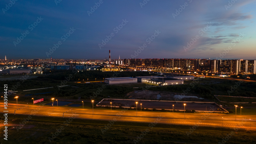 Aerial view of the residential buildings next to bigger highway with many cars and forest in the historical and at same time modern city of St. Petersburg at light summer night