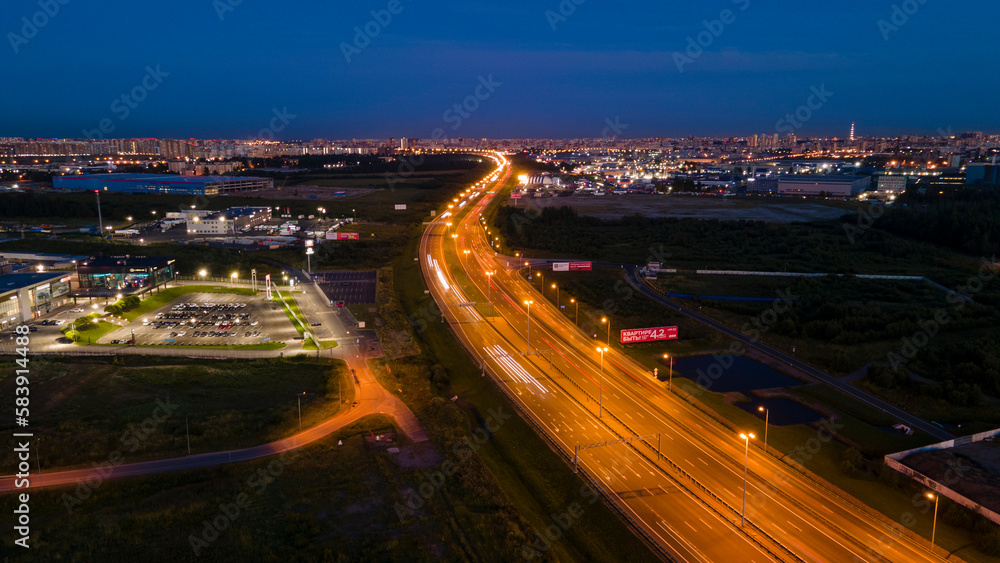 Aerial above view of the bigger highway with many cars next to forest and the historical and at same time modern city of St.Petersburg at light summer night