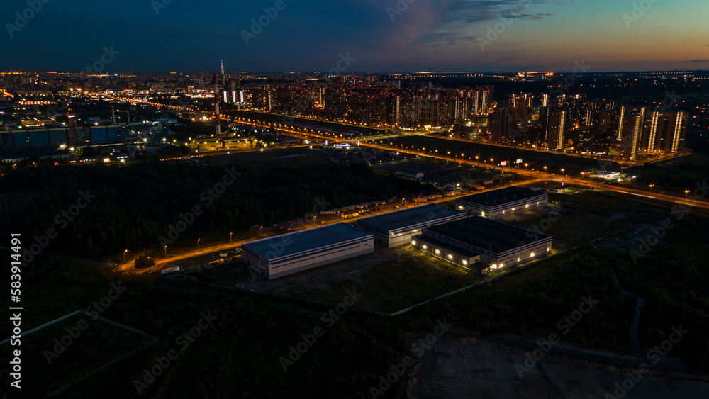 Aerial view of the high-rise buildings next to bigger highway with many cars and forest in the historical and at same time modern city of St. Petersburg at summer night
