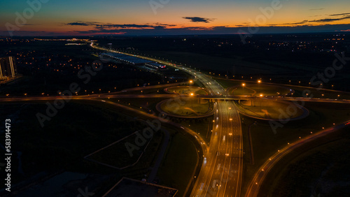 Aerial view of the bigger transportation interchange with many cars next to forest and the historical and at same time modern city of St. Petersburg at light summer night © Alex