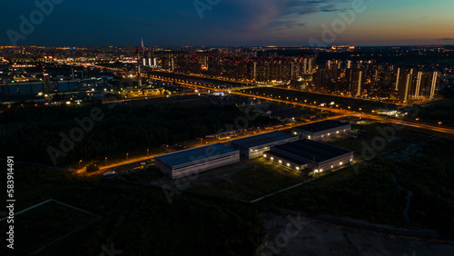 Aerial view of the high-rise buildings next to bigger highway with many cars and forest in the historical and at same time modern city of St. Petersburg at summer night © Alex