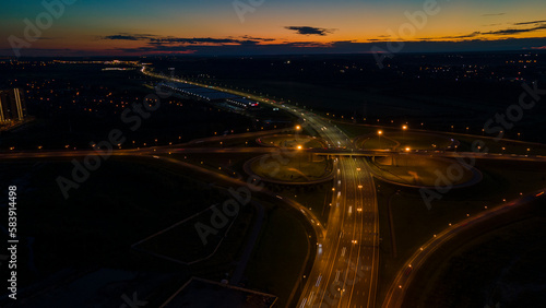 Aerial view of the big traffic interchange with many cars next to forest and the historical and at same time modern city of St. Petersburg at summer night