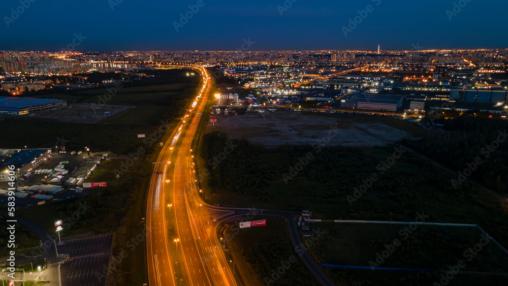 Aerial above view of the bigger highway with many cars next to forest and the historical and at same time modern city of St. Petersburg at light summer night
