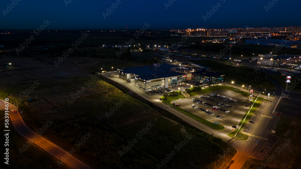 Aerial view of the shops next to bigger highway with many cars and forest in the historical and at same time modern city of St. Petersburg at light summer night