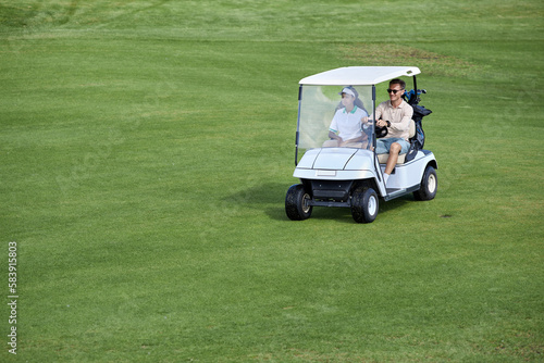Wide angle view of couple driving golf cart on green field minimal, copy space