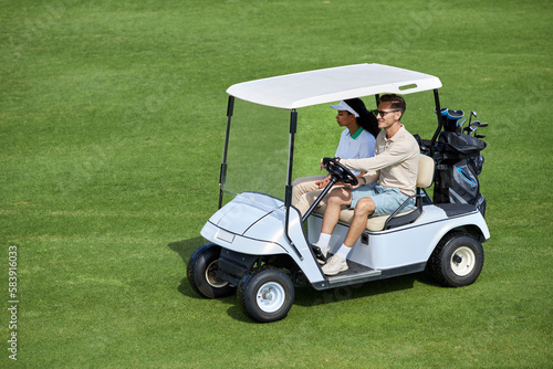 High angle view at sporty couple driving golf cart on green field minimal, copy space
