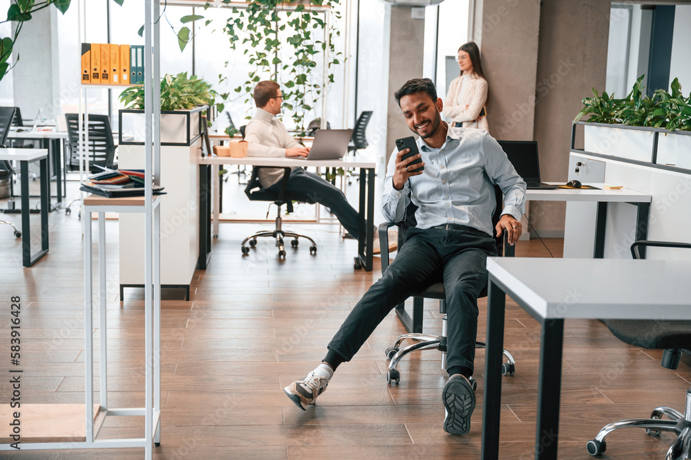 Taking a break. Using smartphone. Men and woman are working in the office together Taking a break. Using smartphone. Men and woman are working in the office together