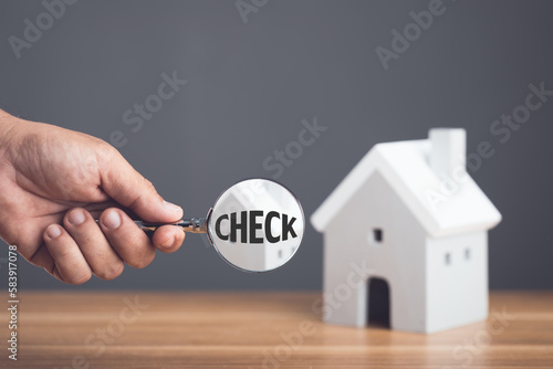 Check before home delivery, Hand holding a magnifying glass and inspecting the house model on wooden desk. The concept of finding home problems before signing a contract.