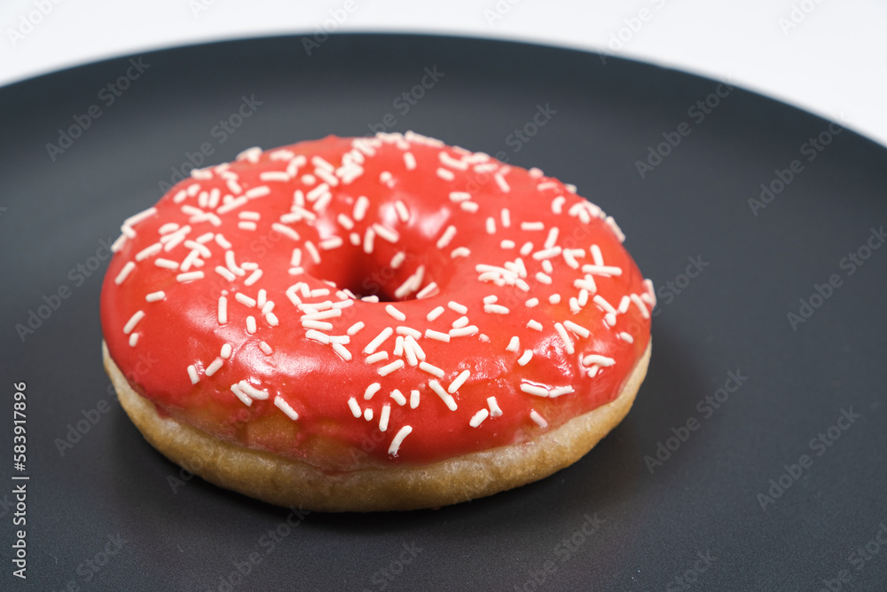 Large doughnut with red glaze and sprinkled on a black background Large doughnut with red glaze and sprinkled on a black background