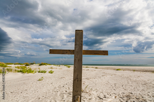 A Christian holy wooden cross on a calm and beautiful beach with ocean waves and dramatic skies in the background