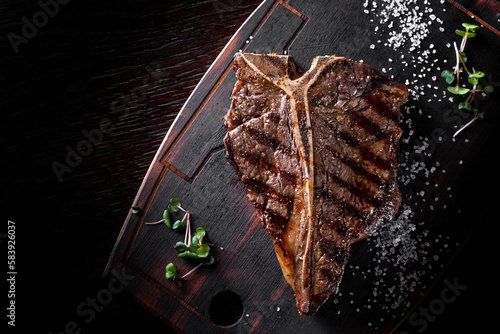 Grilled T-bone Steak on bones on wooden plate on bkack background photo