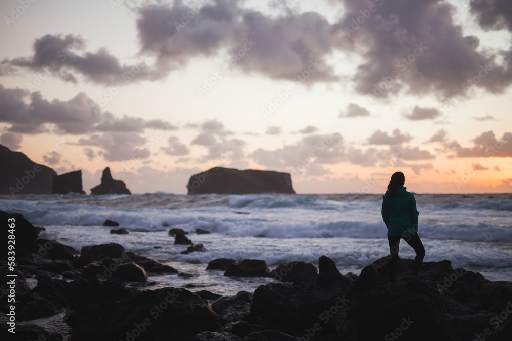Woman standing on rocky seashore at sunset Woman standing on rocky seashore at sunset