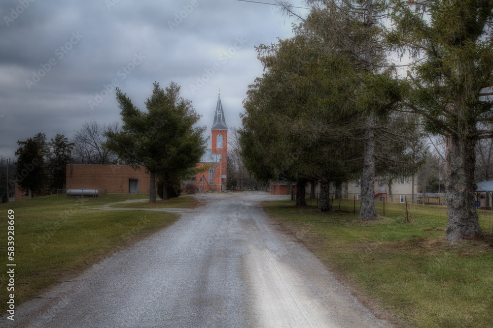 St. Joesph Catholic Church Apple Creek Missouri. A rural Perry County Catholic Church at the end of a gravel road. The Steeple rises between two evergreens. Winter clouds gather above the temple. 