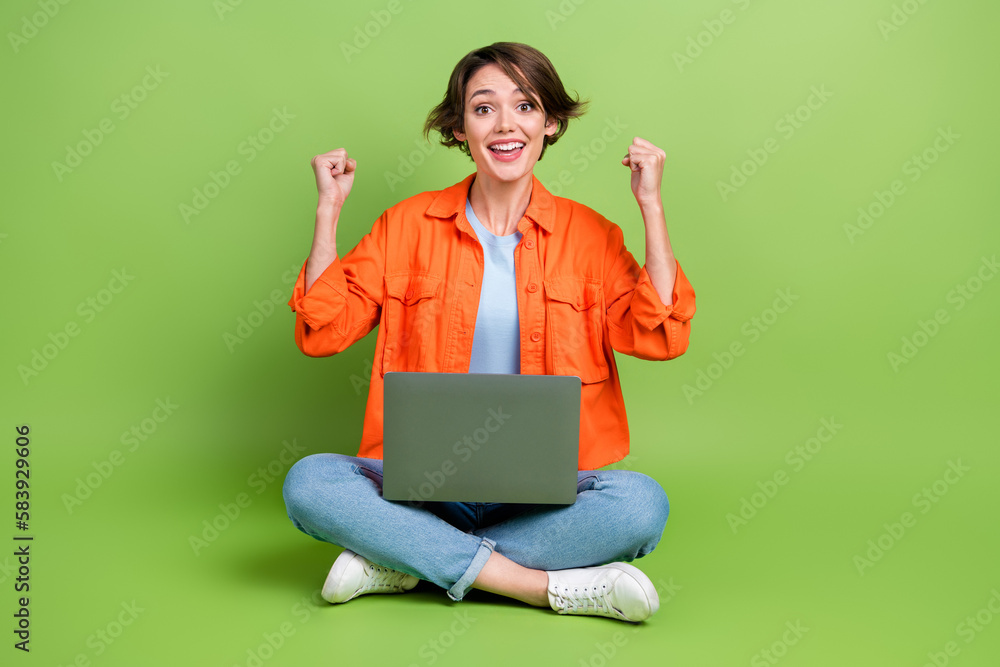 Full length photo of lucky sweet lady dressed jeans shirt wining modern gadget rising fists isolated green color background Full length photo of lucky sweet lady dressed jeans shirt wining modern gadget rising fists isolated green color background