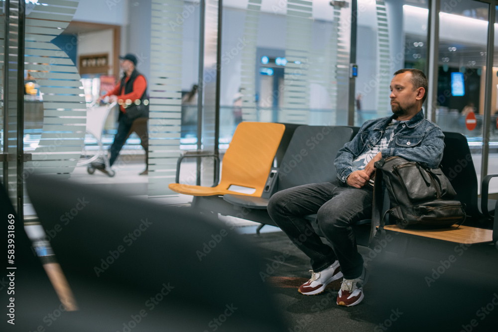 Obraz premium A male passenger is sitting waiting for boarding in the departure area of the modern airport terminal.