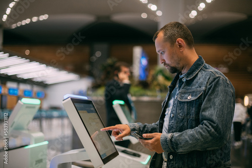 A male passenger at the electronic check-in desk in the departure area of the modern airport terminal. photo
