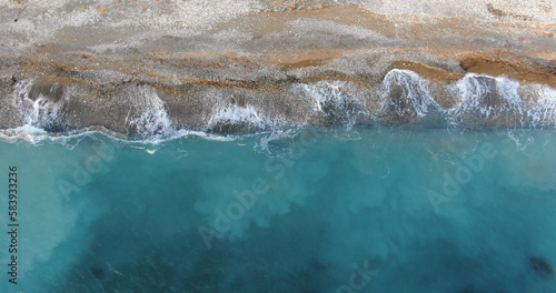 Flying drone over the coastline of the island overlooking rocky shoreline with vegetation and rocks and clear sea with light foamy waves in Cyprus.