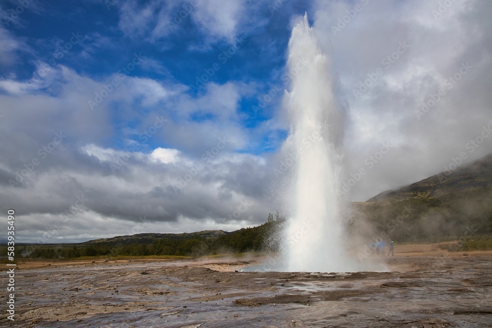 Beautiful view of a Geyser on a rocky land under the blue sky with clouds