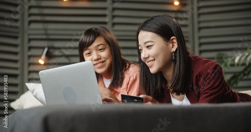 Two asian sisters spending time together, having online shopping, chatting and happily smiling, keying in the credit card - family time, online shopping 