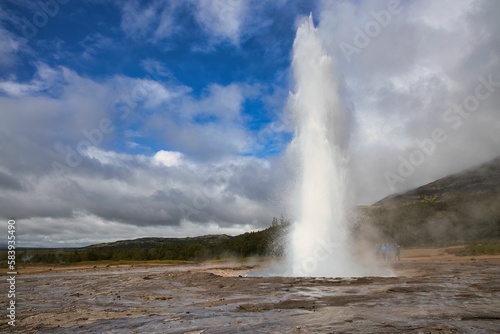 Beautiful view of a Geyser on a rocky land under the blue sky with clouds