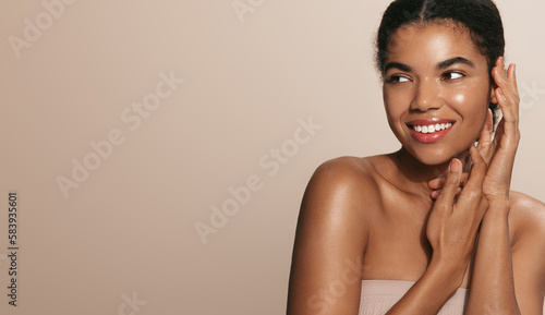 Young african american girl with clear skin, washing her face and body, looking hydrated and nourished, standing over beige background