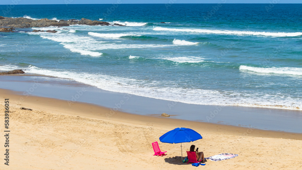 Beach Holiday Girl Umbrella Sitting With Mobile Phone Shoreline With Ocean Waves towards Summer Blue Horizon. Beach Holiday Girl Umbrella Sitting With Mobile Phone Shoreline With Ocean Waves towards Summer Blue Horizon.