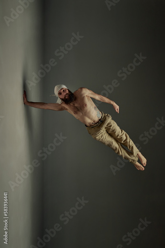 Bearded shirtless man practising yoga, training over dark studio background. Muscular, healthy, fit body shape. Art of movement, male body aesthetics, health, sportive lifestyle concept
