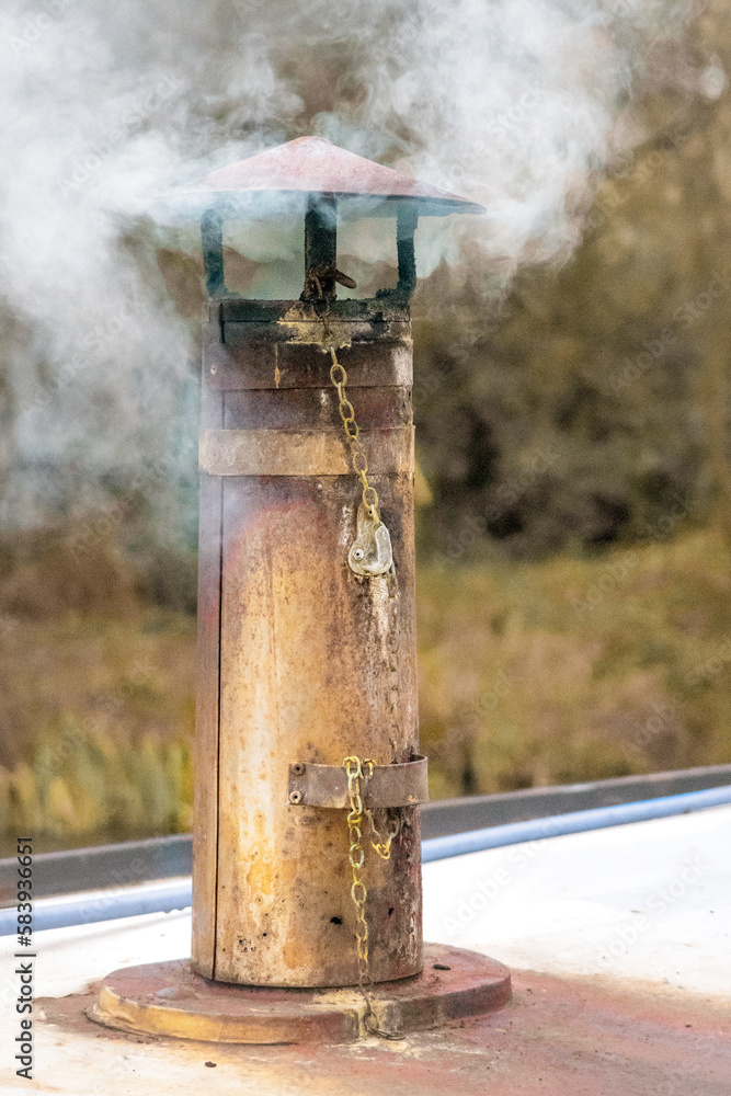 Vertical closeup of smoke coming out of a boat chimney along the Thrupp Canal in Oxfordshire, UK
