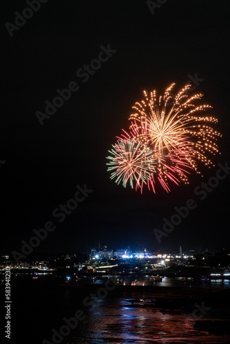 Fireworks during British firework championships exploding over illuminated city Plymouth Cornwall © Pez Photography/Wirestock Creators
