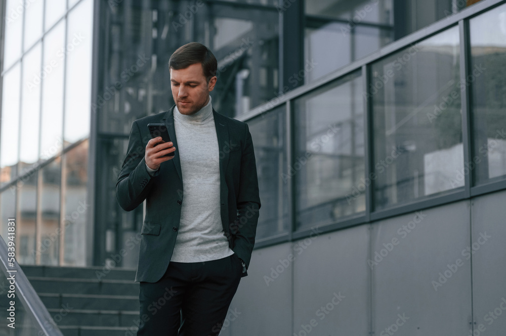 Windows behind the handsome man that is in the formal clothes using smartphone