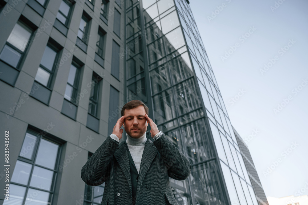 Having headache, feeling bad, stressful. Handsome man in formal clothes is outdoor near the business building Having headache, feeling bad, stressful. Handsome man in formal clothes is outdoor near the business building