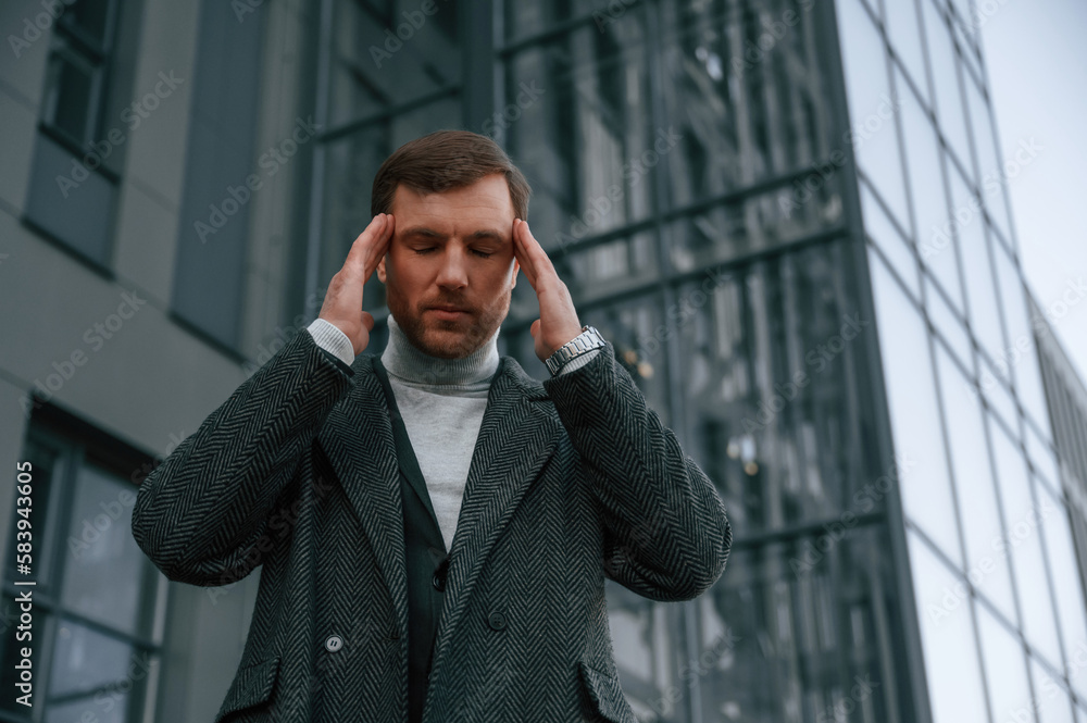 Having headache, feeling bad, stressful. Handsome man in formal clothes is outdoor near the business building Having headache, feeling bad, stressful. Handsome man in formal clothes is outdoor near the business building