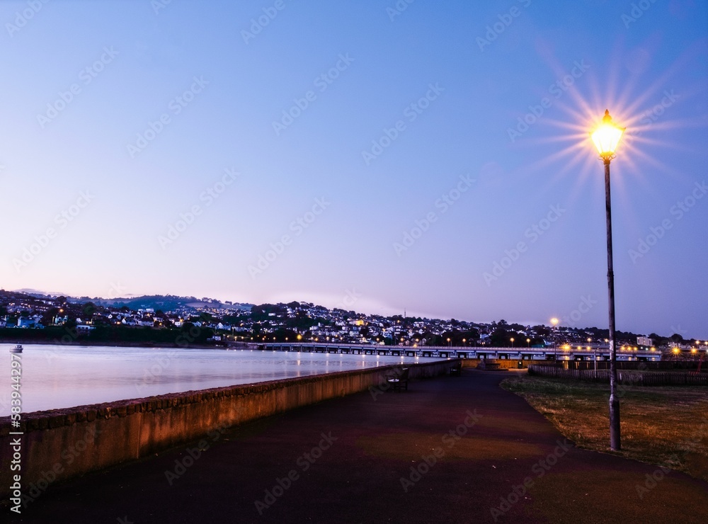Illuminated street lantern shining next to the river Teign against the purple sky in Shaldon Devon