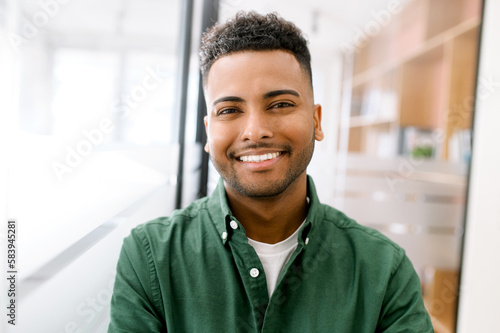 Close-up portrait of a happy indian young man with friendly wide toothy smile, latin guy wearing casual ggreen shirt looks into camera, employee profile photo