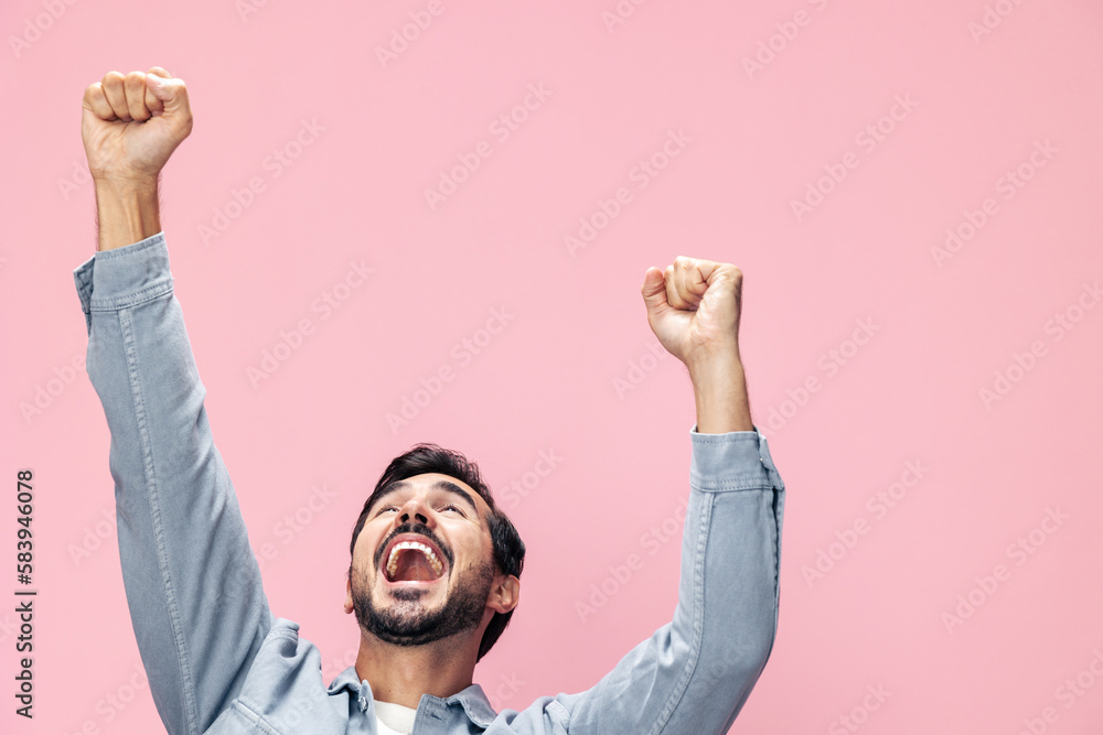 Fashion portrait of a brunette man with a beard happiness victory raised his hands with his fist up on a pink background in a white T-shirt smile and joyful emotion on his face, copy space